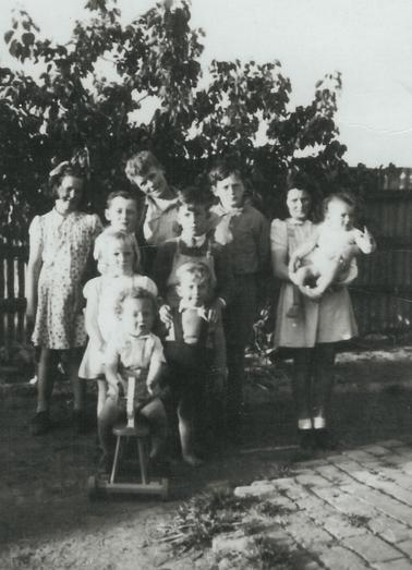 Black and white photograph of 10  children of various ages.  One child holding a baby. One child on wooden bicycle. List of names attached.