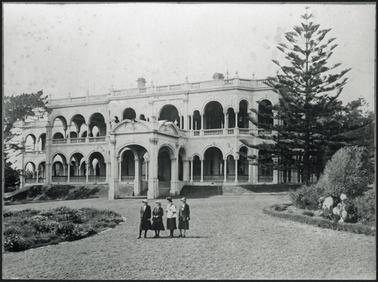 Italianate two storey stuccoed mansion, with established gardens, four people in driveway 