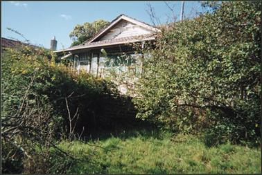 The image is of a c1920s weatherboard cottage, hipped tiled roof, set in an unkempt garden