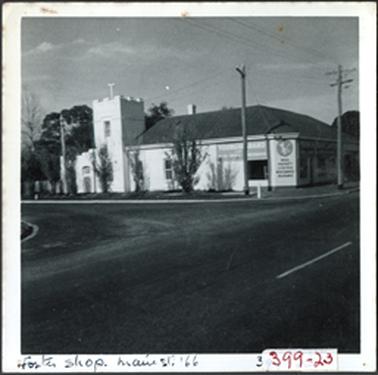 A corner hipped roof shop with castle style section on left, part two storey stuccoed brick, advertising on wall