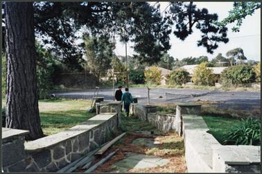 At ‘CraigieLea’ a view to the tennis court (bitumenised) via half walled walkway/steps, on left mature pine tree