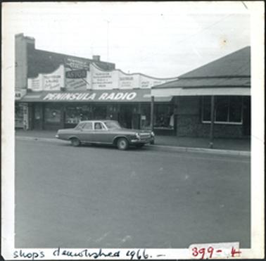 Shop with verandah and fluted upper facade, on right hipped roof house/shop with verandah, tiled front on left 2 storey building