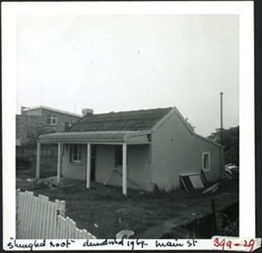 This image is of a hipped and skillioned cottage with a shingled roof a bull nosed veranda, stucco brick
two external chimneys and a central front door