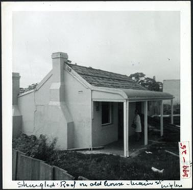 This image is of a hipped and skillioned cottage with a shingled roof a bullnosed veranda and a semi sided view of the house with two external chimneys