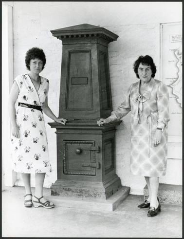 Mrs Joan Bognuda and Mrs Leslie Moorhead posing for a photograph outside the Old Post Office, Mornington and standing beside the old cast iron letter box