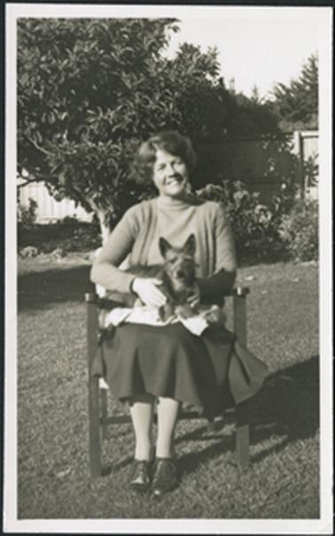 Portrait of a young woman seated in a chair in a garden with a small terrier dog seated on her lap