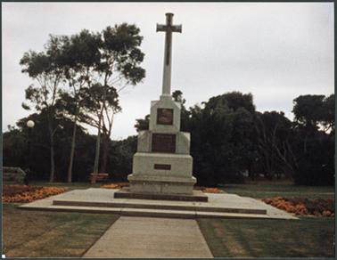 A front image of the World War 1 and 2 Memorial with floral arrangements at edges and mature trees in the background