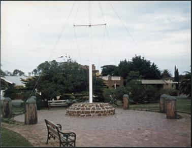 Image of a flagpole the base of which is constructed of stone and cemented onto a paved area the flag pole is painted white