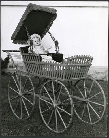 A close up view of the antique pram with its sun roof extended and opened a doll dressed in period costume is seated in the pram