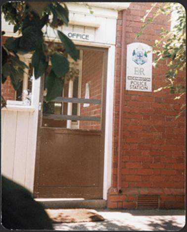 Front Entrance of Police Station showing fly wire door and brick wall with ‘Police Station’ sign