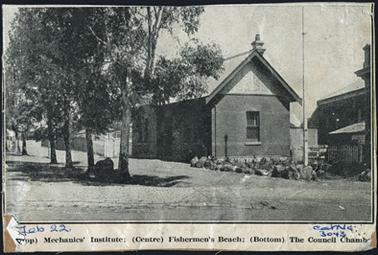 Exterior view of the Council Chambers depicting a single storey red brick building with a steep pitched iron roof a flag pole is situated out the side of the building with a series of gum trees out the front