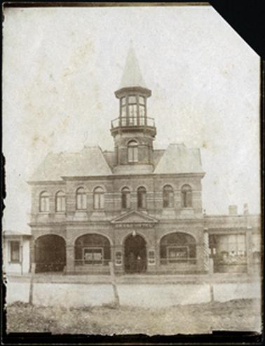 Front facade of the Grand Hotel a two storey building with tower, with Mansard French Renaissance revival rooves windows in the tower. Eight arched windows on top floor, a gabled pediment over its door, the basket arched windows either side of the door looked into the bar