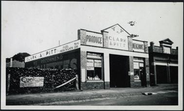 The image shows the front facade of the brick building used by Clark & Pitt, Produce (Fuel) Merchants attached to the building is a bell tower on the right and stacked fuel to the left of the building several signs advertising   briquettes, coke etc. also to the right of the image is another shop front c1945