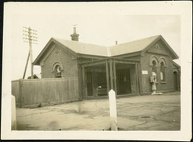 A front view of the Mornington Post Office with a wooden picket fence out the front of the building facing Main Street the old style weighing machine is situated at front of the building on the Esplanade side