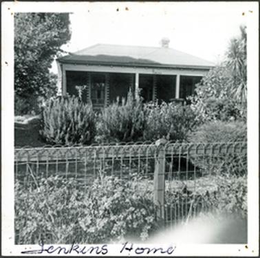A double fronted house with hipped roof and wire fence house almost hidden by established garden