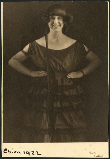 A smiling image of Monica with her hands on hips, looking towards photographer, wearing 1920's outfit