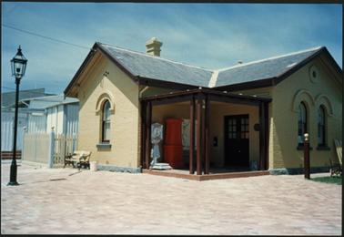 This view shows the front entrance to the Old Post Office Museum with the painting and paving work completed
street lamp shown in the left hand side of the photo, wooden seat positioned against wall of building and weighing scales in the foyer