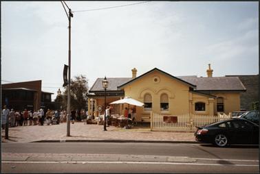 The image shows the OPOM on the corner of Main Street and the Esplanade, Mornington, with Book Stall in front and to the left of the photo people waiting for the celebrations