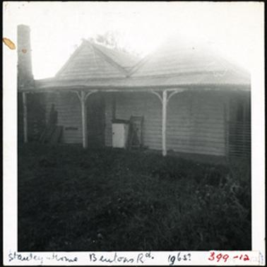 A wooden building with hipped roofs and verandah one chimney at the left of the building
