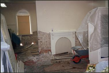 The image shows work being done to treat the rising damp around the window and the fireplace