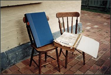 Display of newspapers to be repaired “opened at the Post “ and sample of repaired newspapers in folder displayed on chairs outside OPOM