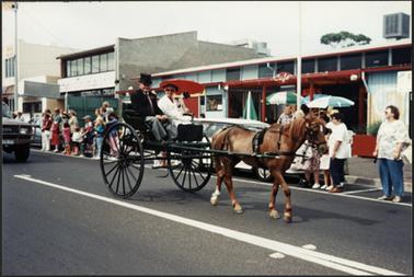 Colour image of an Australia Day event depicting a horse and gig being driven past the “Burnt Toast Cafe” in Main Street Mornington the occupants of the gig are Gwen Jordan and Lindsay Freth dressed in costume