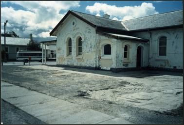 A side on view of the Old Post Office Museum 1987, showing the side entrance, and preparation being undertaken before repainting of the building. Work is being undertaken on the concrete area in the front of the building which would result in a paved and grassed area