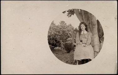 The image is of Leila Steedman sitting on a chair beside a tree in a garden setting, oval photo