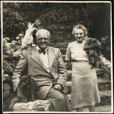The image is of Hunter and Hilda Rogers on a stone stepped walkway, with them are their pets, Susie and Bunty (dogs) and pet cocky
