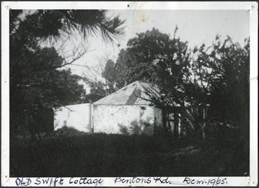 A side view of the building which has hipped roofs and extended back building partly hidden by trees
