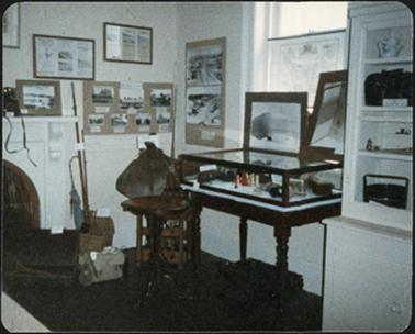 Photographic and picture displays on wall and mantelpiece with a display cabinet to the right of photo at the OPOM Mornington