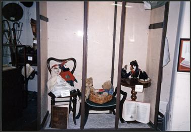 Heritage Week display of dolls and teddy bears and the black Easter hens, to left of display are hats and umbrella stand