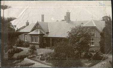 The house has Queen Anne revival attributes, single-storeyed and verandahed, built from coloured brickwork, with a hipped and slated roof - established garden in foreground