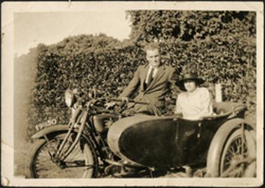 The image shows a male person sitting on a motorcycle with Wyn Bradford sitting in side car