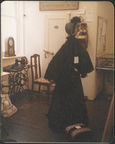 A display which includes clock, sewing machine, chair and ladies' period costume