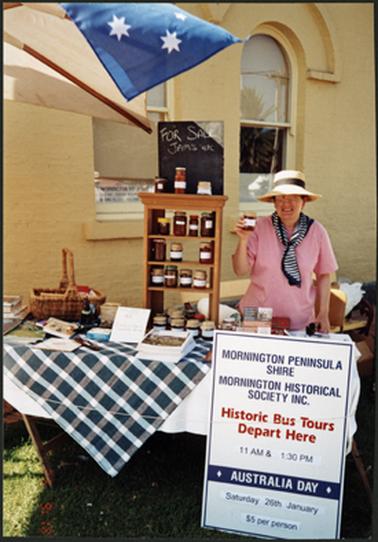 Chris Platt behind a stall selling jams, pickles and other items outside OPOM Australia Day 2002
In front of the stall a sign advertising Mornington Peninsula Shire ‘Historic Bus Tours Depart Here’