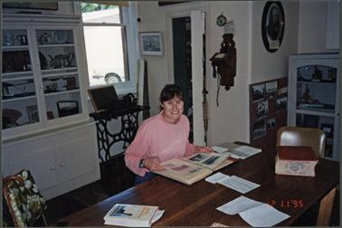 Maureen Tregonnning , in the Post Office Museum, studying photo album, in background display cabinet,
Singer sewing machine, and wall telephone