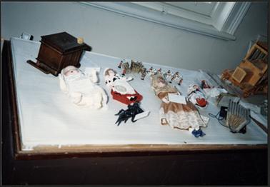 On display for Heritage  Week 1991 at the Old Post Office Museum, a doll collection including a baby doll, French doll, wax doll, a miniature coach and horses, and child’s piano accordion
