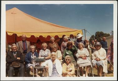 A group of thirteen people from the Stone-Young family photographed in front of a yellow marquee
