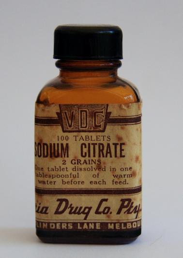 Brown glass bottle with black bakelite screw lid.  Cream and black manufacturer’s Label on front of bottle (cream and black).