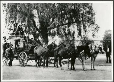 The image is of a mail coach with team of horses, a coach driver and eleven other people on board or standing beside the coach, perhaps passengers
