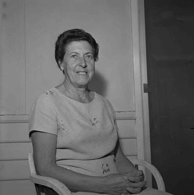 Portrait of a seated woman with short dark hair, wearing a pale short sleeved dress.