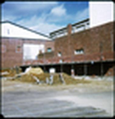 This shows the rear of a red brick building, which is being altered. It has an industrial appearance. There is scaffolding in the foreground, and a pile of rubble and builders sand too. 