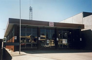 The Mornington Fire Station is a smart rectangular building of one storey. It has three bays with glazed doors and a fire truck can be seen in each of the three bays. The CFA logo sits at the centre of the fascia. A concrete apron lies to the front and there is a metallic tower at the rear for the siren. The blank side wall of a two storey building is on the right. 