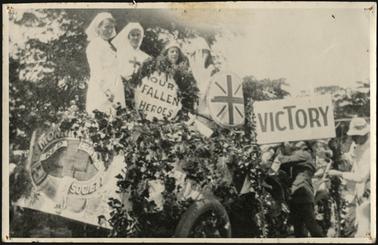 The image is of the Mornington Red Cross Society Members on a decorated vehicle celebrating Victory, a sign reads 'Our Fallen Heroes', in photo M. Jenkins, J. Olley, V. Blacker, R. Bates