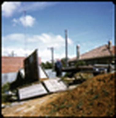 This photograph shows two men lifting corrugated iron fencing. In the foreground is a pair of beautiful old panelled doors which have obviously been ripped out during this renovation work of the shops.
