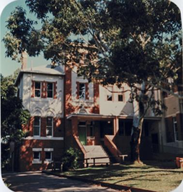 This is a view of a different part of the facade of the Convent of Mercy to that in item 1294. Here the centre piece is a three story tower of red brick with white rendering with a flight of steps leading to a green door and set just in front of the two wings of a three story building. A substantial eucalypt tree stands in a small lawn at the front of the building.