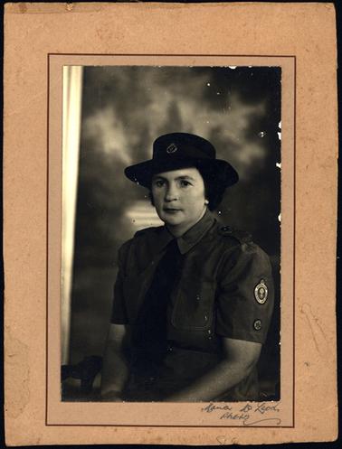 This shows a good looking dark haired woman wearing a uniform and hat. The insignia badge on the sleeve states: Australian Women’s Land Army. There is a sheaf of wheat pictured in the centre of the badge.