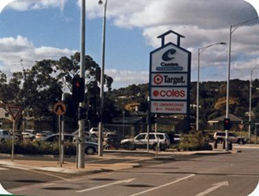 A busy junction of Barkly Street with roadways into and out of the Centro Mornington Shopping Centre.  It is just to the west of the site where the Railway Gate House once stood. The entrance is through car parks and there is a large sign identifying the shopping centre and advertising the major supermarket occupants.Beyond car park to the east are houses among the trees on Beleura hill.