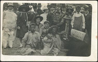 A group of men in fancy dress, sign reads 'Votes For Women'